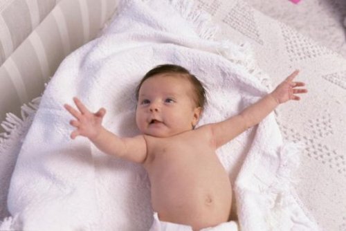 Baby liegt im Bett und streckt Arme in die Luft.