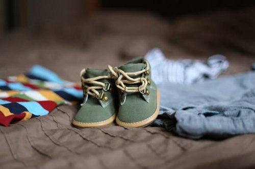 Kleine Babyschuhe liegen auf Klamotten.