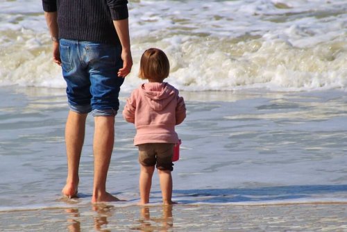 Vater steht neben Tochter am Strand.